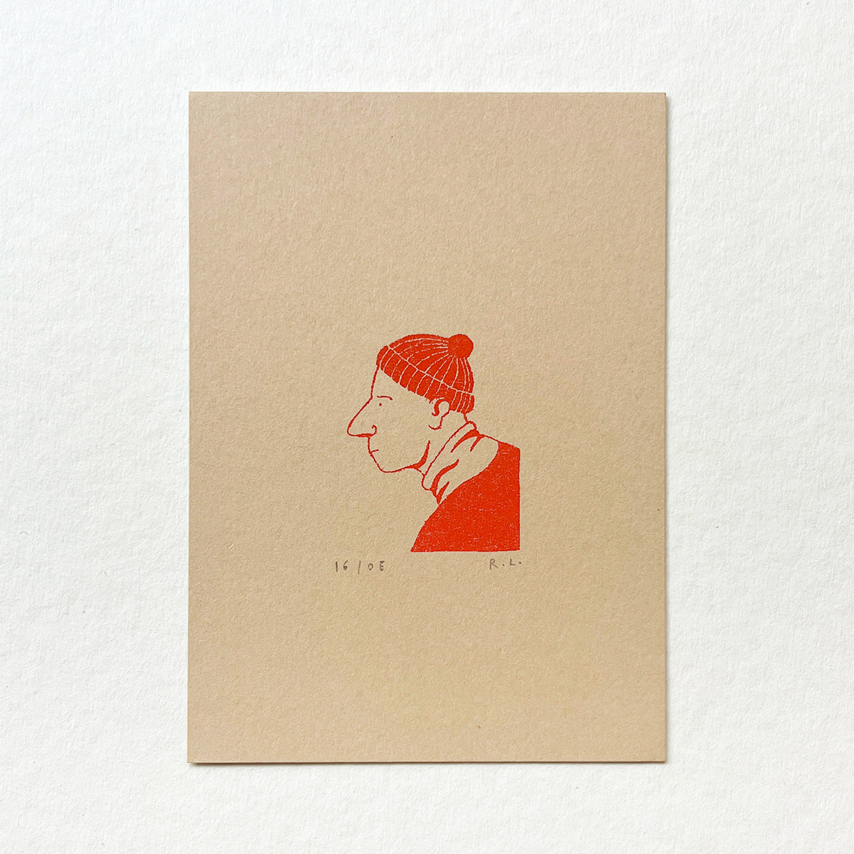 A square art print on textured beige paper featuring a minimalist red ink illustration of a man in profile wearing a knit beanie, displayed against a clean white background.