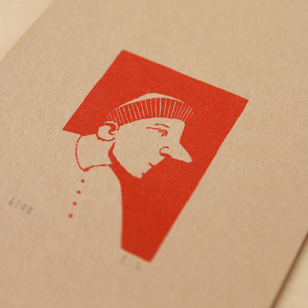A close-up of a textured kraft paper surface featuring a minimalist red graphic print of a stylized face profile with a beret hat.