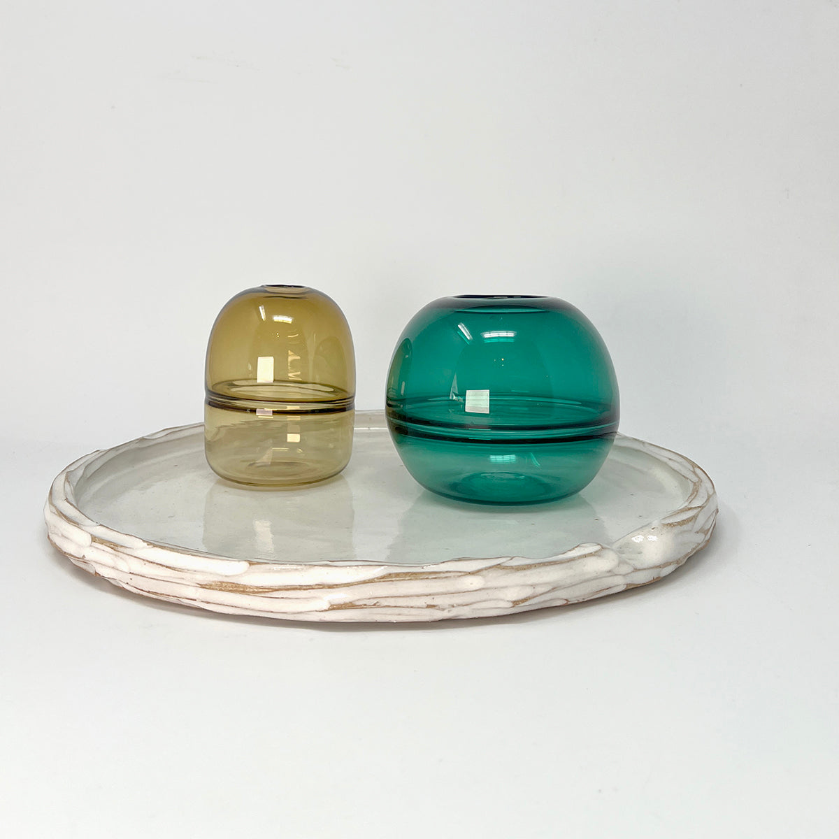 Simple carved white glazed ceramic platter, with indent for thumb, styled with two glass bud vases in green shades. 