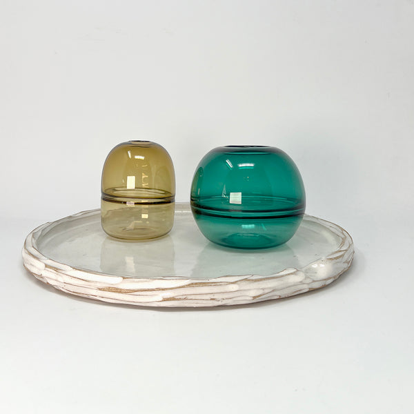 Simple carved white glazed ceramic platter, with indent for thumb, styled with two glass bud vases in green shades. 