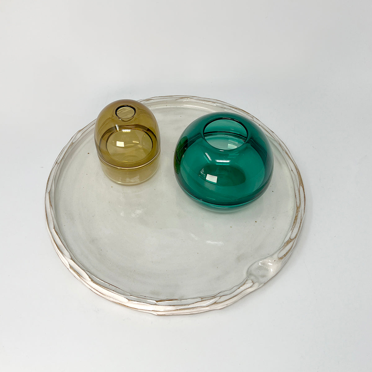 Simple carved white glazed ceramic platter, with indent for thumb with two green glass bud vases. 