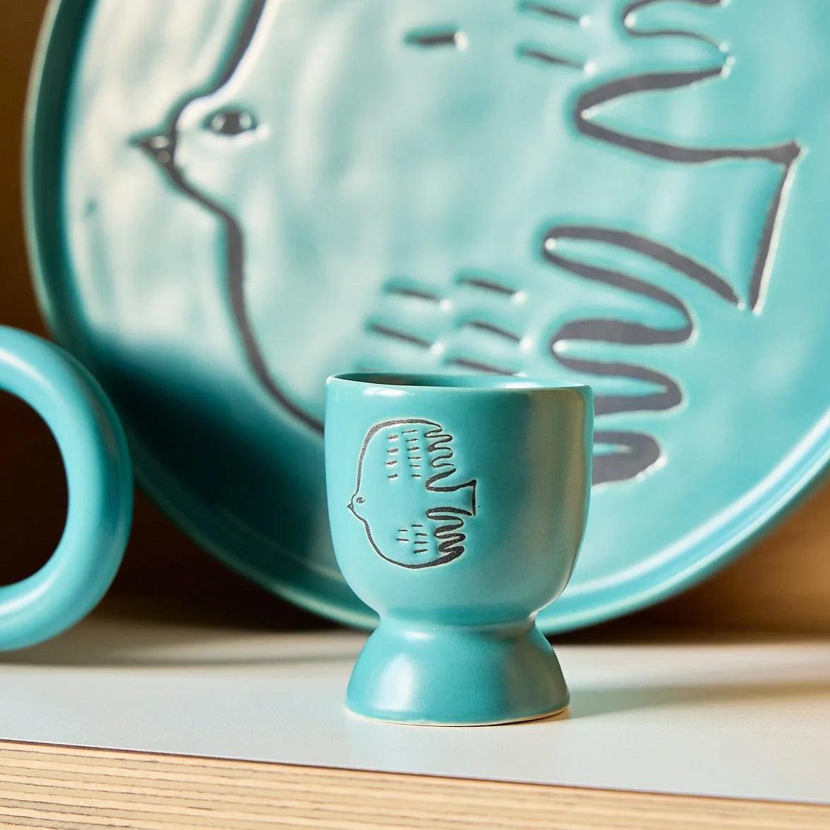 ceramic teal blue egg cup with bird design  sitting on a shelf with a plate in the background