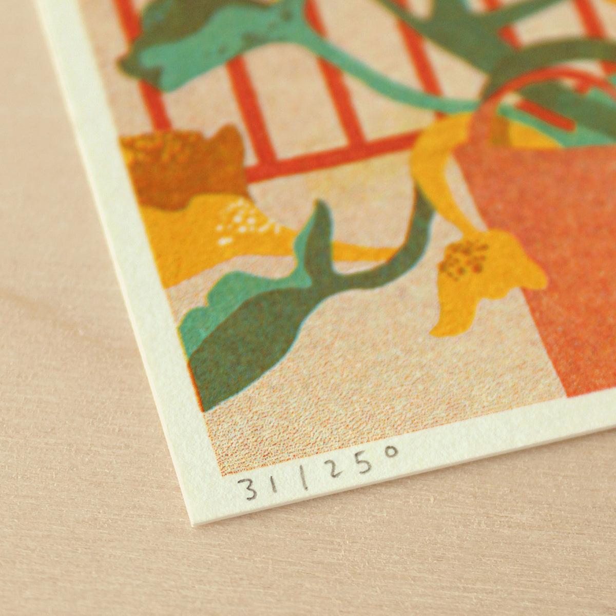 Close-up of a card with a colorful design featuring plants and a red structure on a beige background.