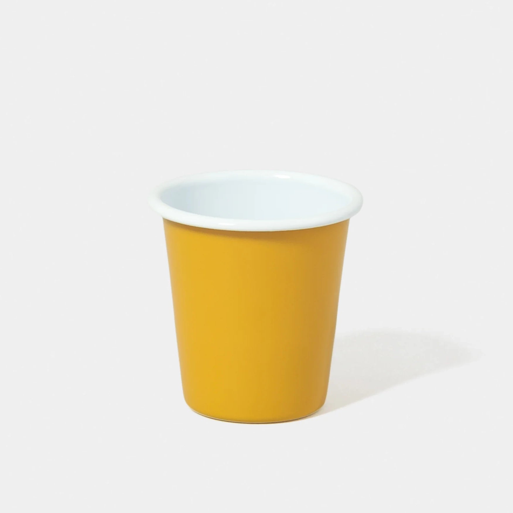 Mustard yellow falconware enamel tumbler with white rim on white background. 