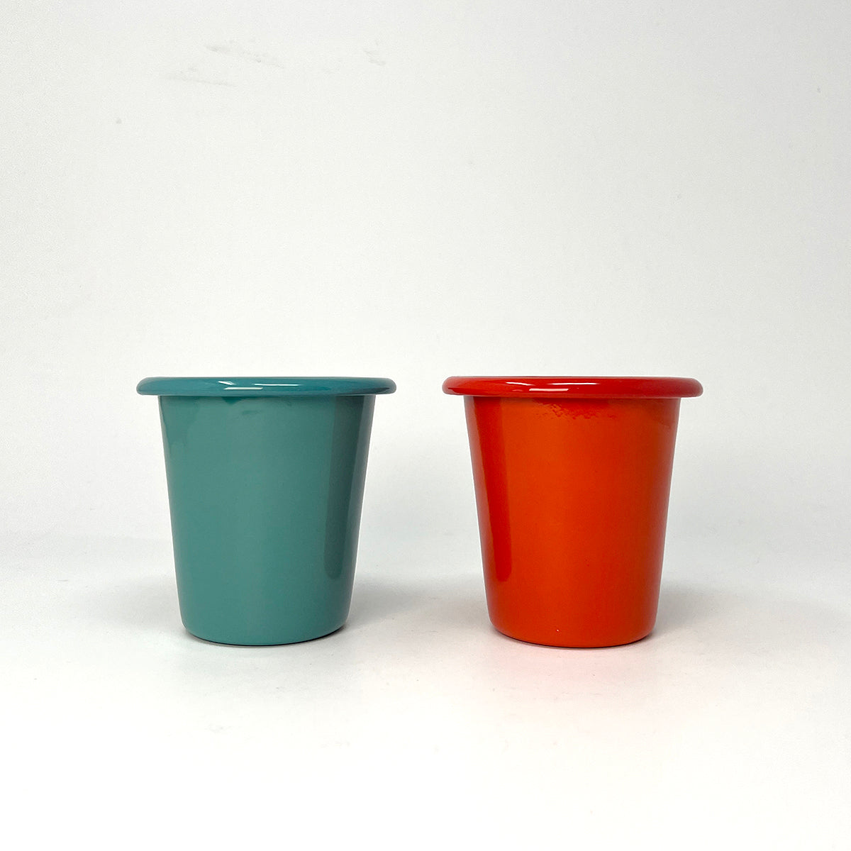 Two enamel tumblers, one teal and one red, on a white background