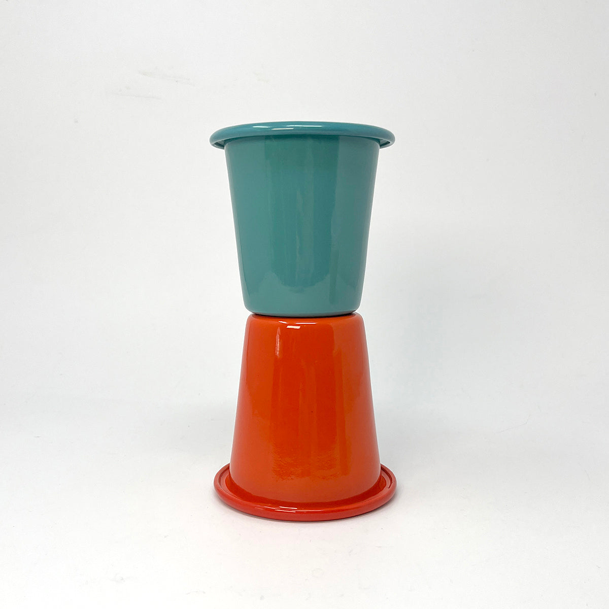 Two enamel tumblers, one teal and one red, stacked on a white background
