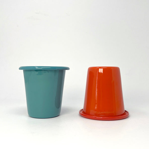 Two enamel tumblers, one teal and one red, on a white background