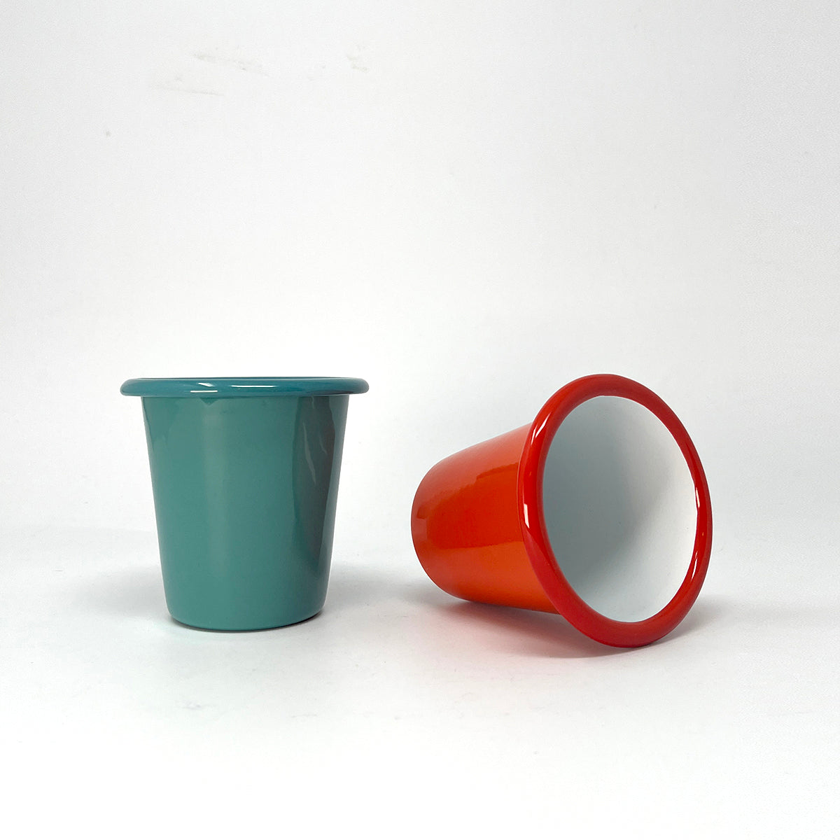 Teal enamel tumbler and red cup with white interior on a white background