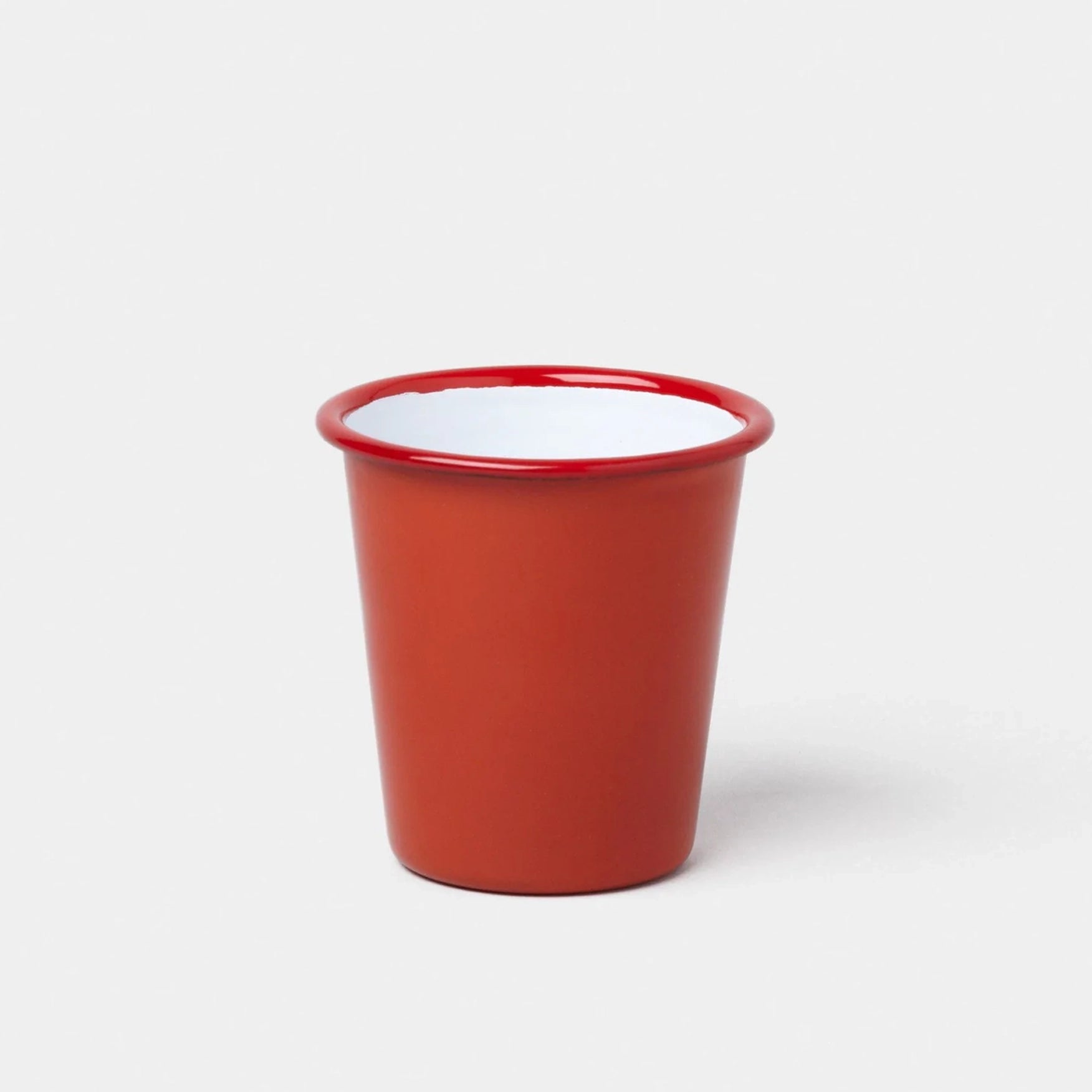 Red enamel tumbler, with white interior, on white background. 