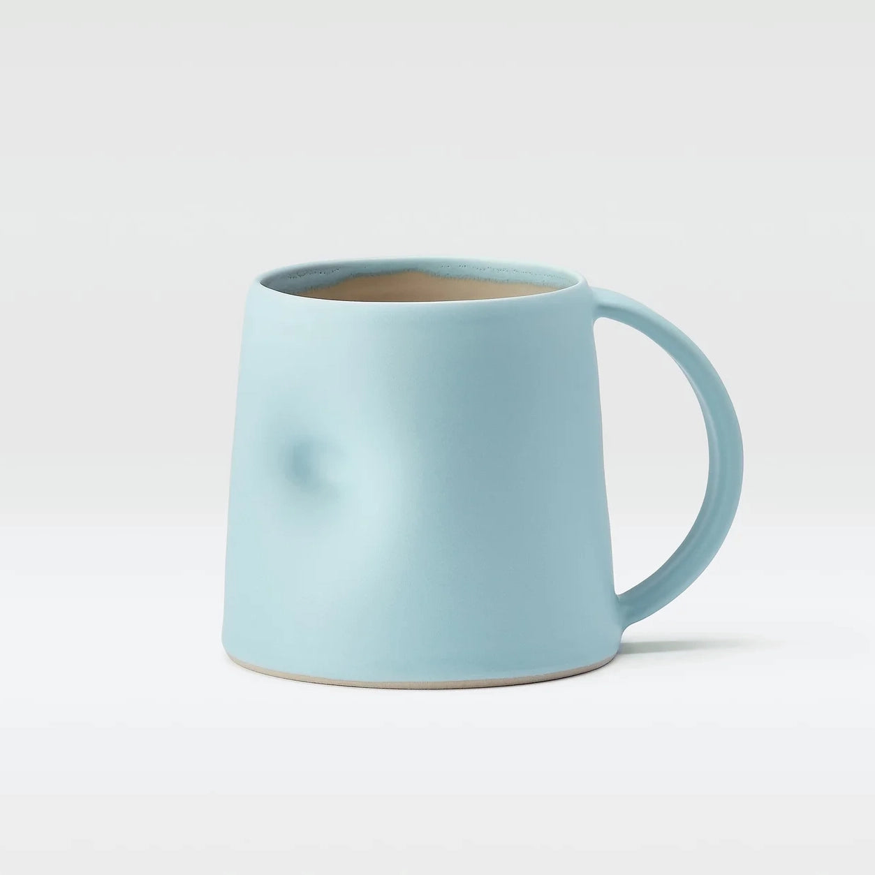 Light blue Emma Lacey hand thrown mug, with a thumb dimple on a white background