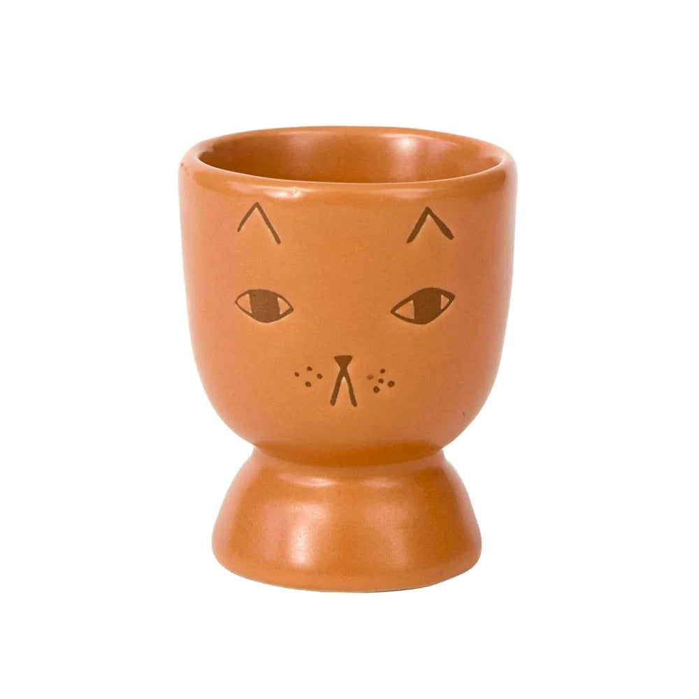 A terracotta-colored ceramic cup shaped like a stylized cat face, featuring simple black line drawings of eyes, whiskers, and ears on a plain white background.