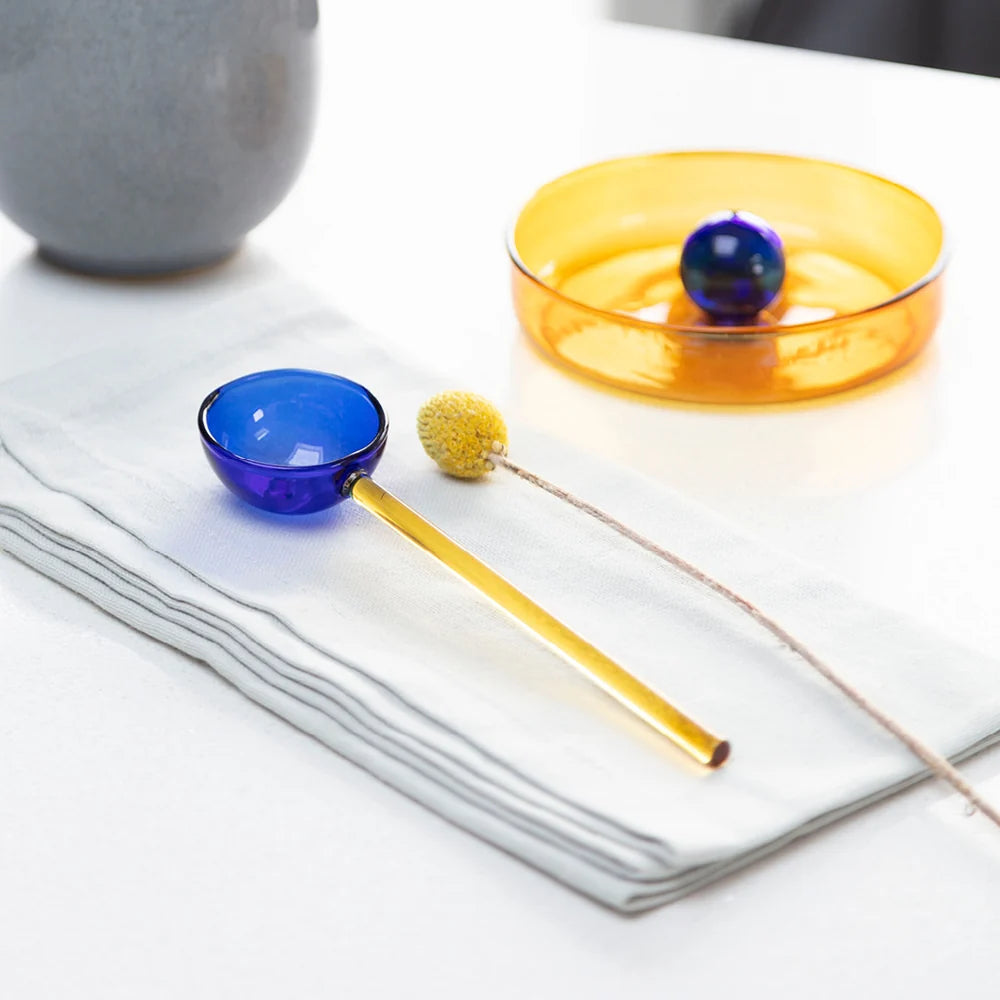 Blue and yellow glass stirrer on a white napkin with a yellow dish in the background