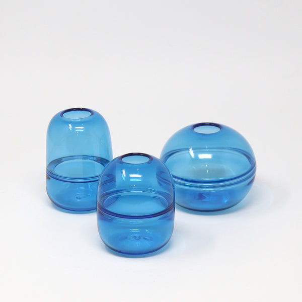 3 aquamarine blue hand blown glass bud vases on a white background by Emma Baker. 