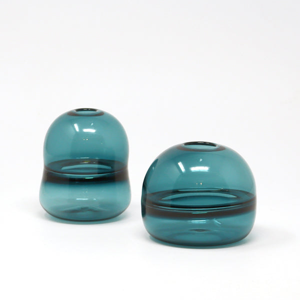 Two teal hand blown glass bud vases on a white background