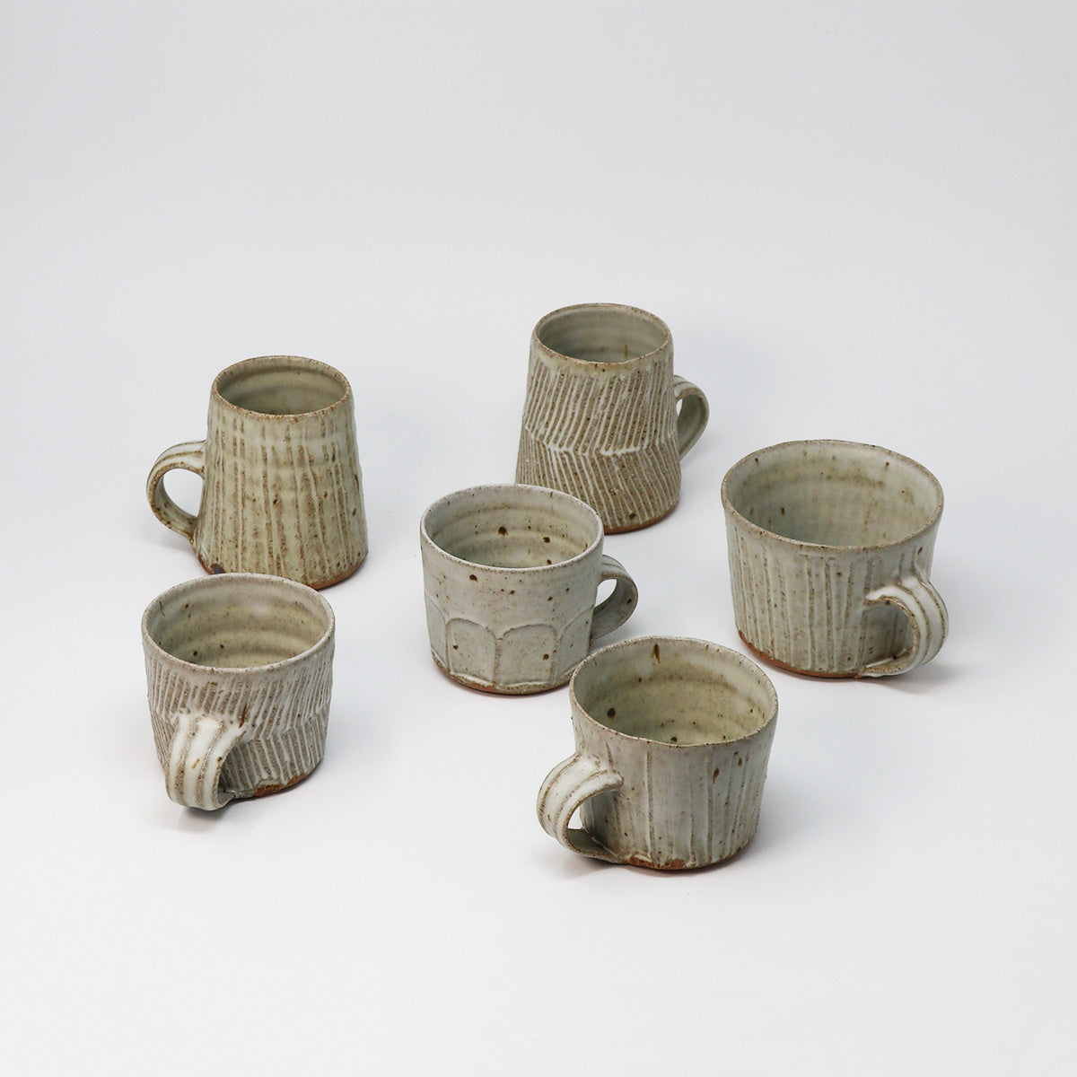 Six handmade ceramic mugs with textured vertical ridges and rustic handles, arranged on a clean white studio background.