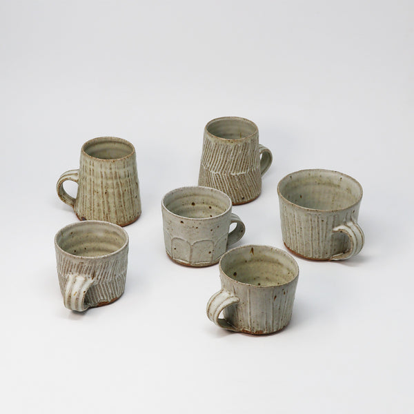Six handmade ceramic mugs with textured vertical ridges and rustic handles, arranged on a clean white studio background.