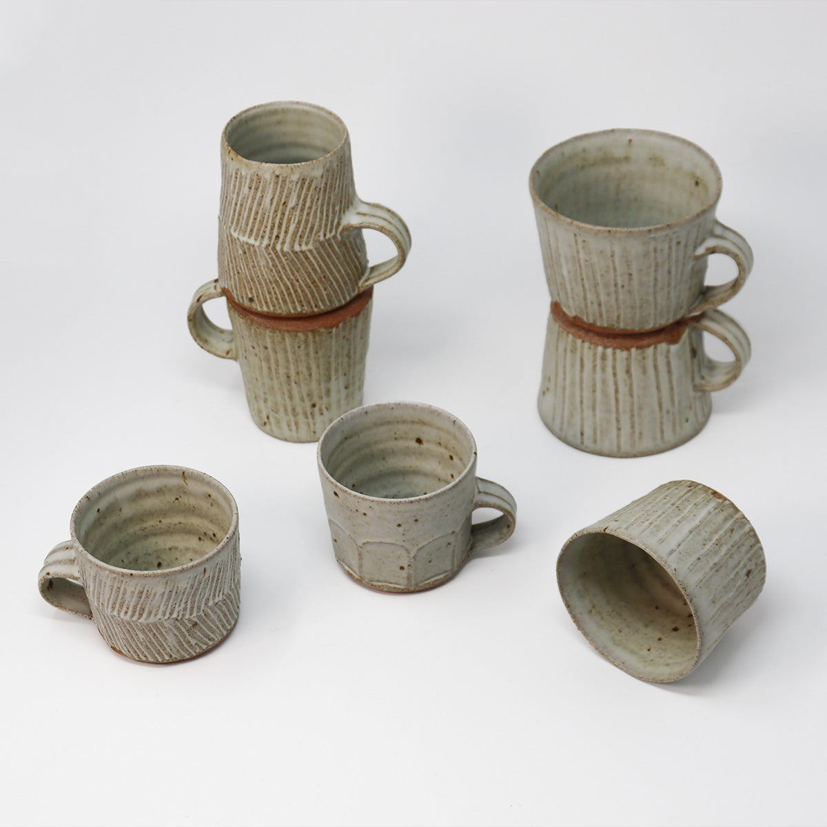 Six handmade ceramic mugs with textured, ribbed surfaces and a speckled off white glaze, arranged on a clean white background.