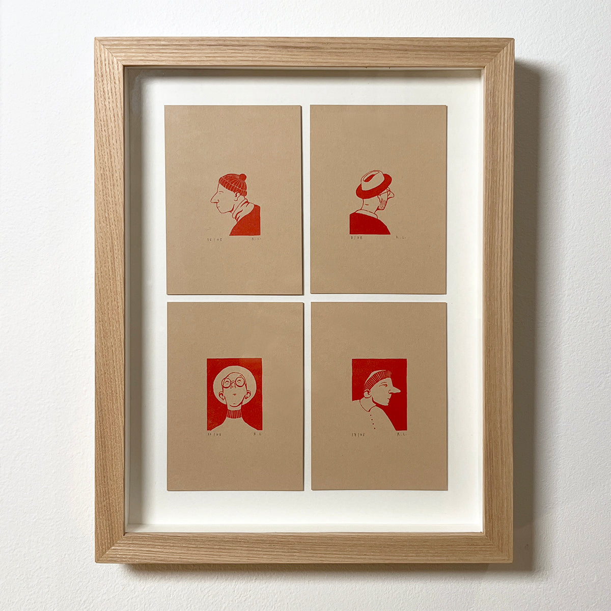 Framed artwork with four red portraits of people wearing different hats on beige paper against a white background
