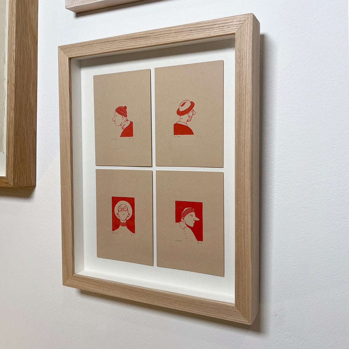 Framed artwork with red illustrations of 4 men wearing hats on beige paper against a white wall.