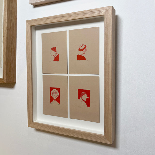 Framed artwork with red illustrations of 4 men wearing hats on beige paper against a white wall.