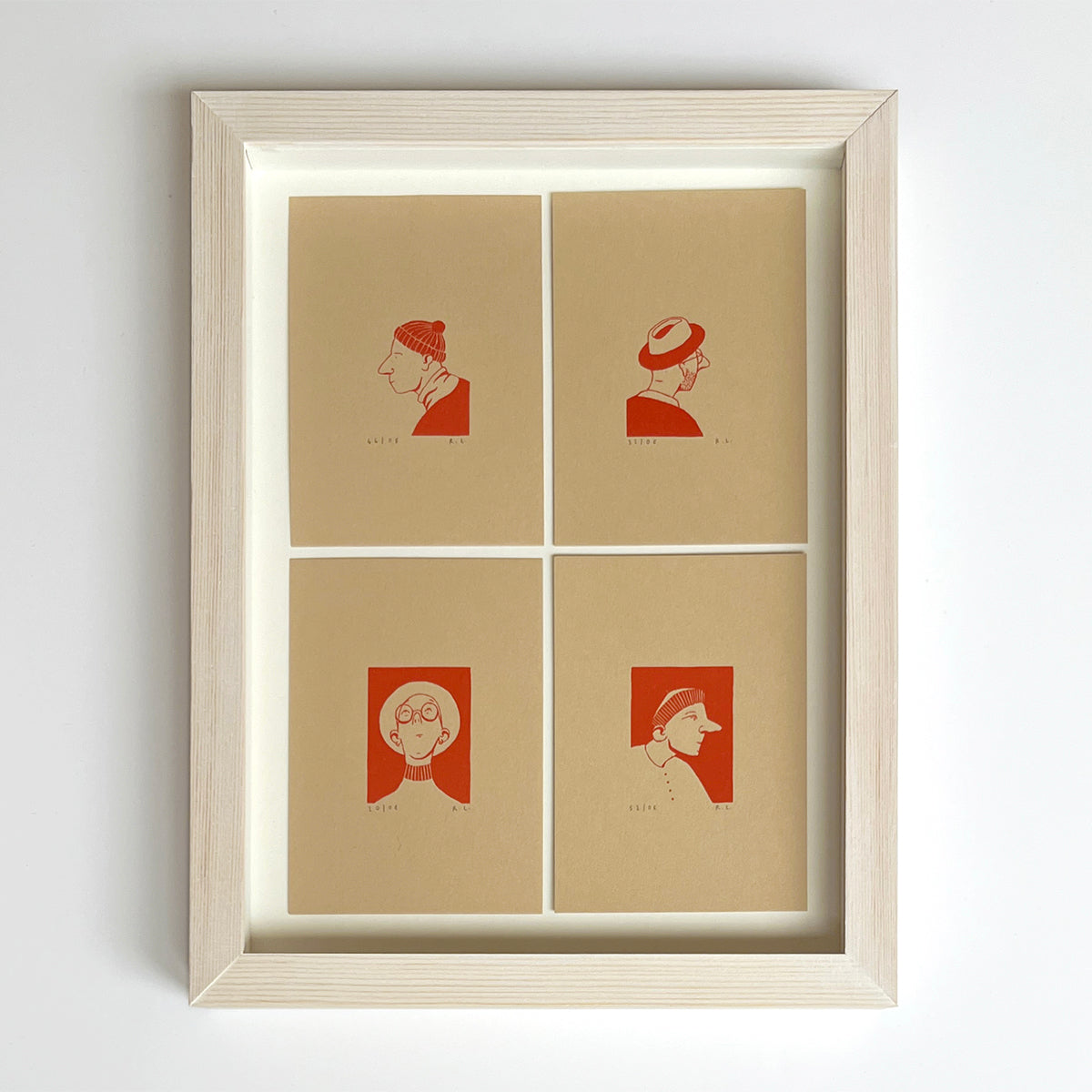Framed four-panel art print with minimalist red profile illustrations of people in hats on beige paper, set in a light natural wood frame against a white wall.