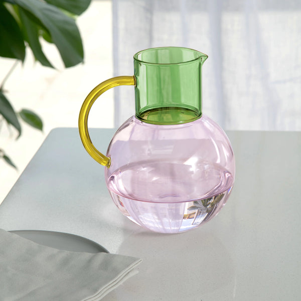 Glass pitcher with green top and yellow handle on a light surface