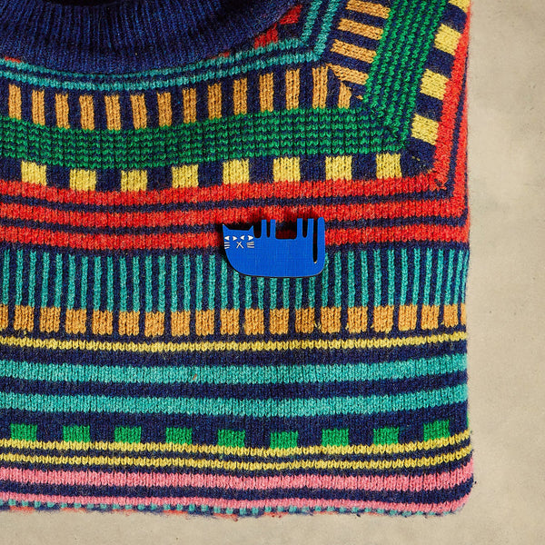 Colorful stripey knitted jumper with a blue cat illustrated pin badge on a beige background