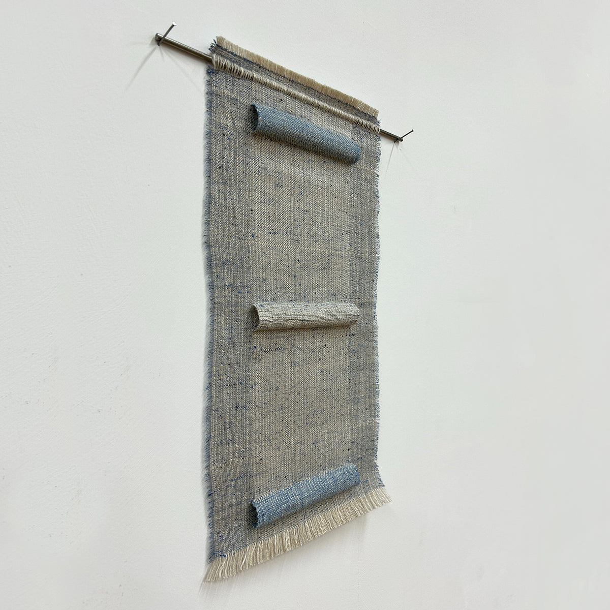 Woven textile art piece with horizontal sections on a white background, hung on a stainless steel rod. 