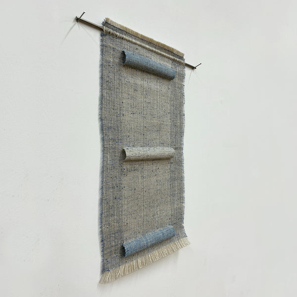 Woven textile art piece with horizontal sections on a white background, hung on a stainless steel rod. 