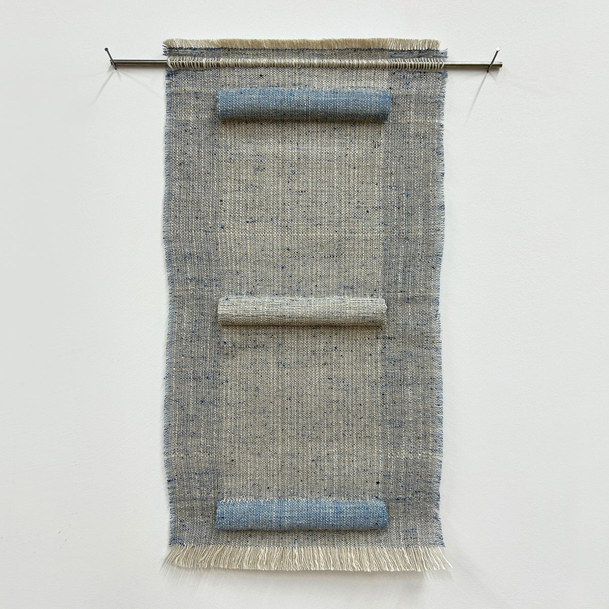 Woven textile art piece with horizontal sections on a white background, hung on a stainless steel rod. 