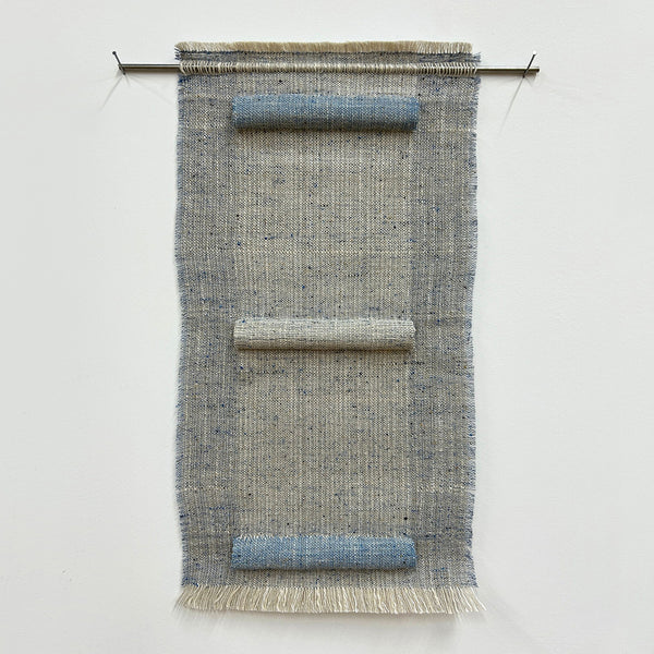 Woven textile art piece with horizontal sections on a white background, hung on a stainless steel rod. 