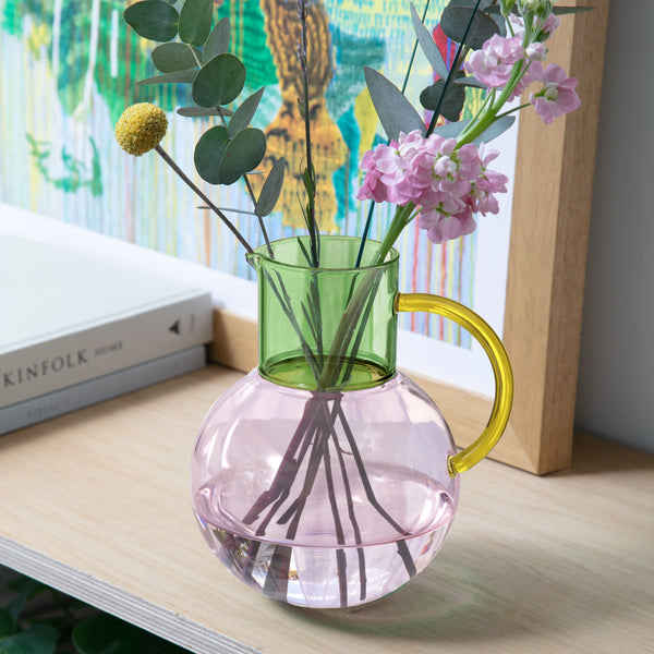 Multicolored glass jug with flowers on a wooden surface