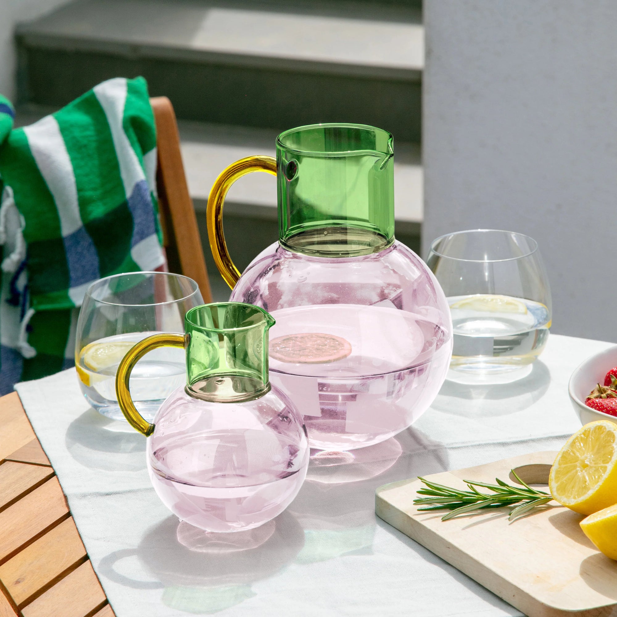 Colorful glass pitchers and glasses on a table with lemons and a towel in the background