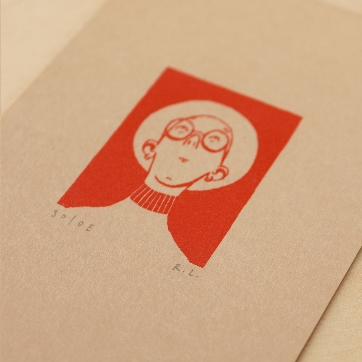 A close-up of a textured kraft paper card featuring a minimalist red graphic print of a person wearing a panama hat inside a red square.