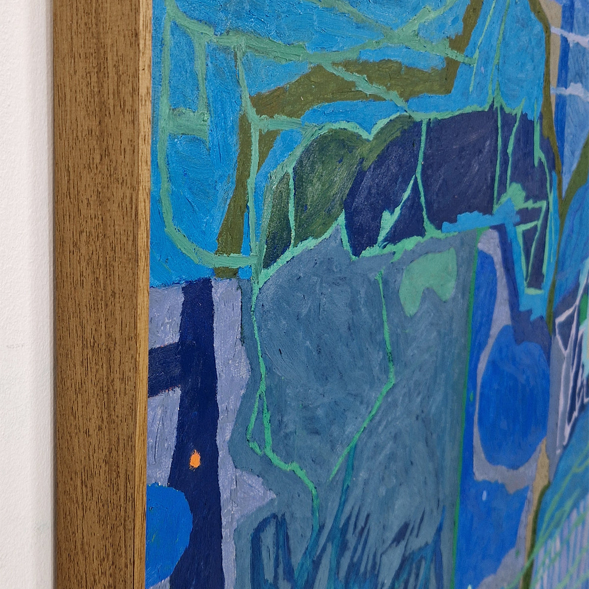 Close-up of an abstract painting featuring textured brushstrokes in shades of blue, navy, green, and gray, bordered by a light brown wooden frame against a white wall.