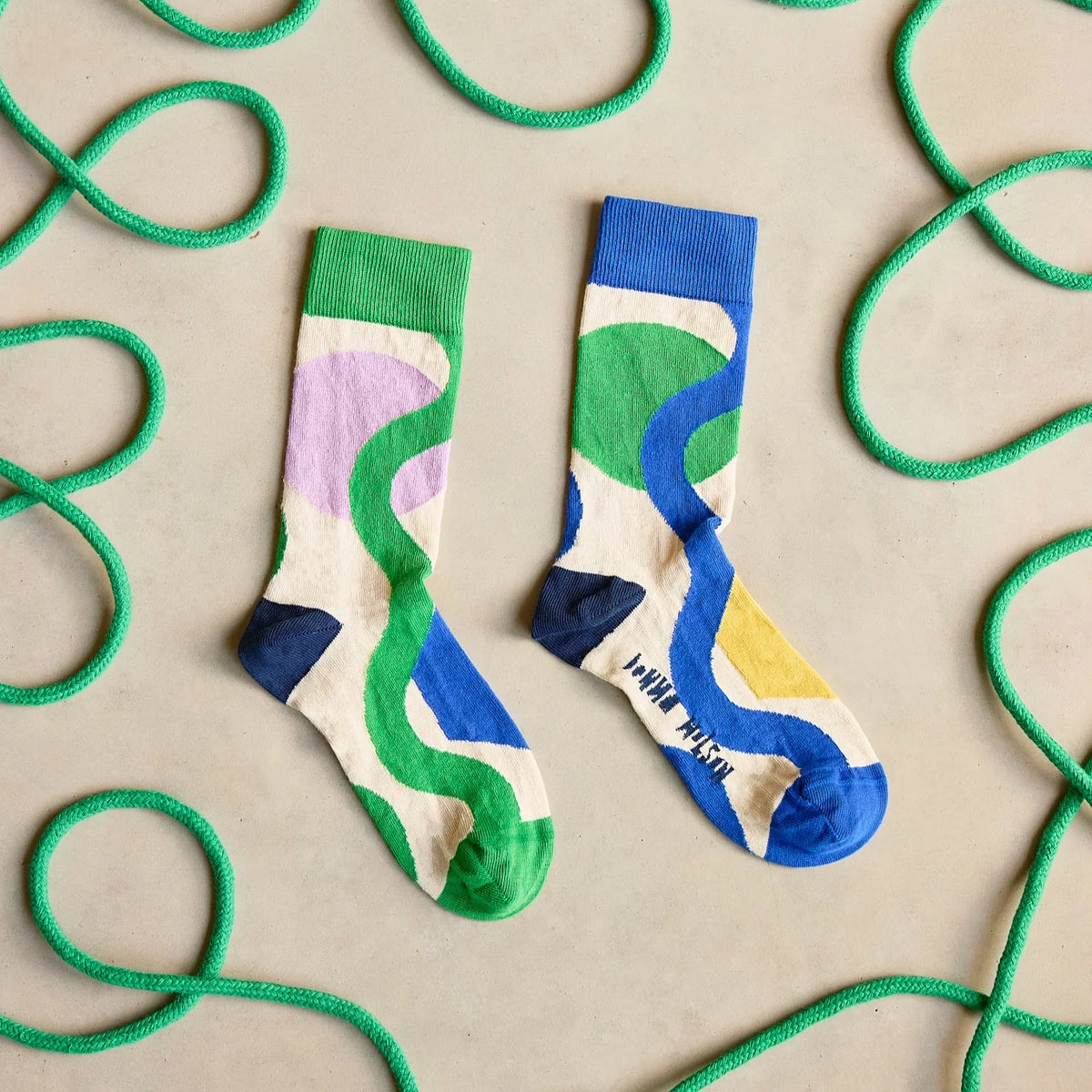Colourful socks with abstract patterns on a beige background with green rope.