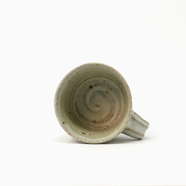 A handmade ceramic cup with a spiral pattern inside, featuring a light neutral glaze with brown speckles, shown from a top-down angle on a white background.