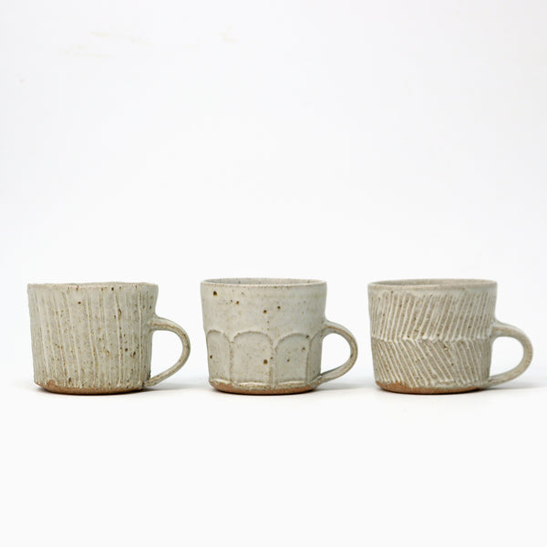 Three small handmade ceramic mugs with textured glazes in a speckled beige and off-white finish, arranged side by side on a white background.