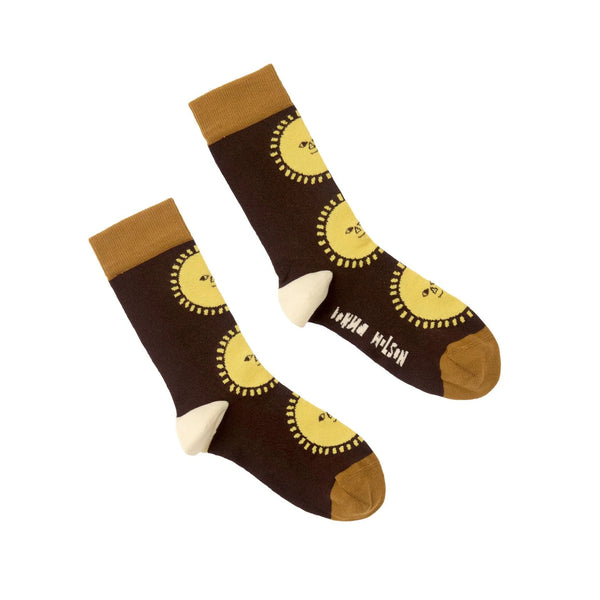 A pair of dark brown crew socks with a repeating yellow sun face pattern, tan cuffs and toes, and white heels, displayed on a clean white background.