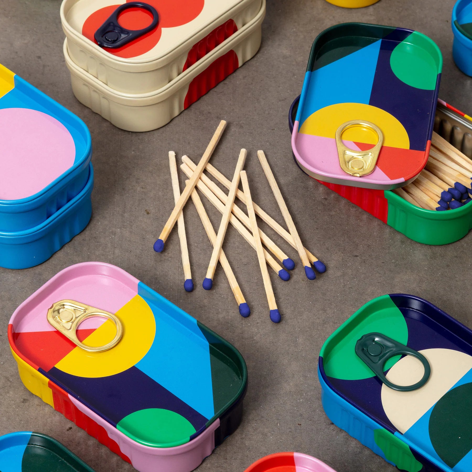 Matches and colourful tins on a grey surface.
