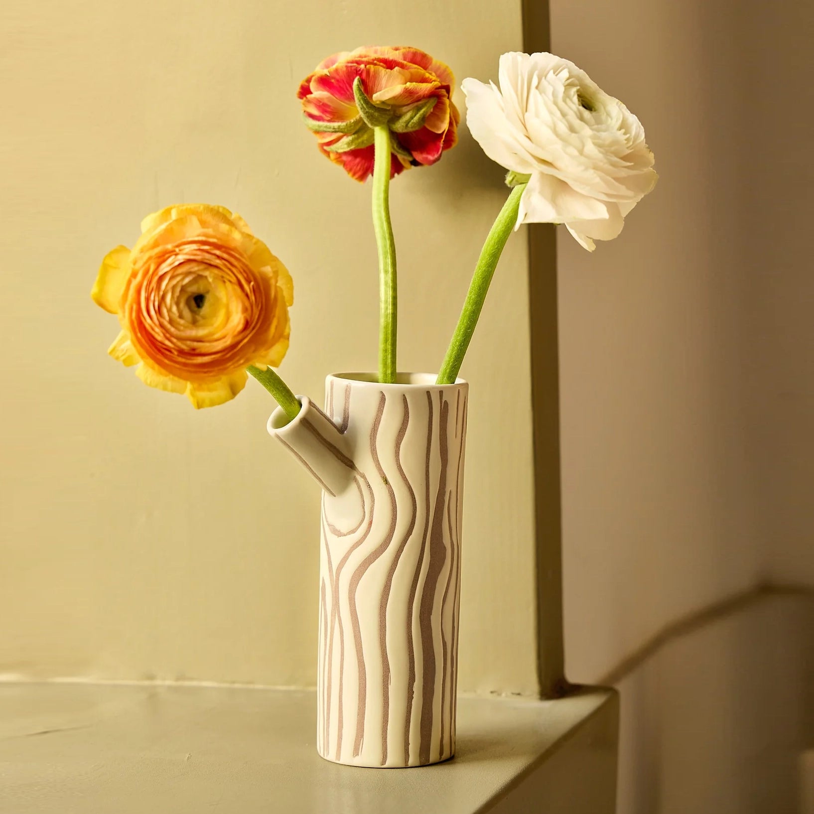 Brown and beige vase in the shape of a log with a tree bark design with three roses on a yellow background