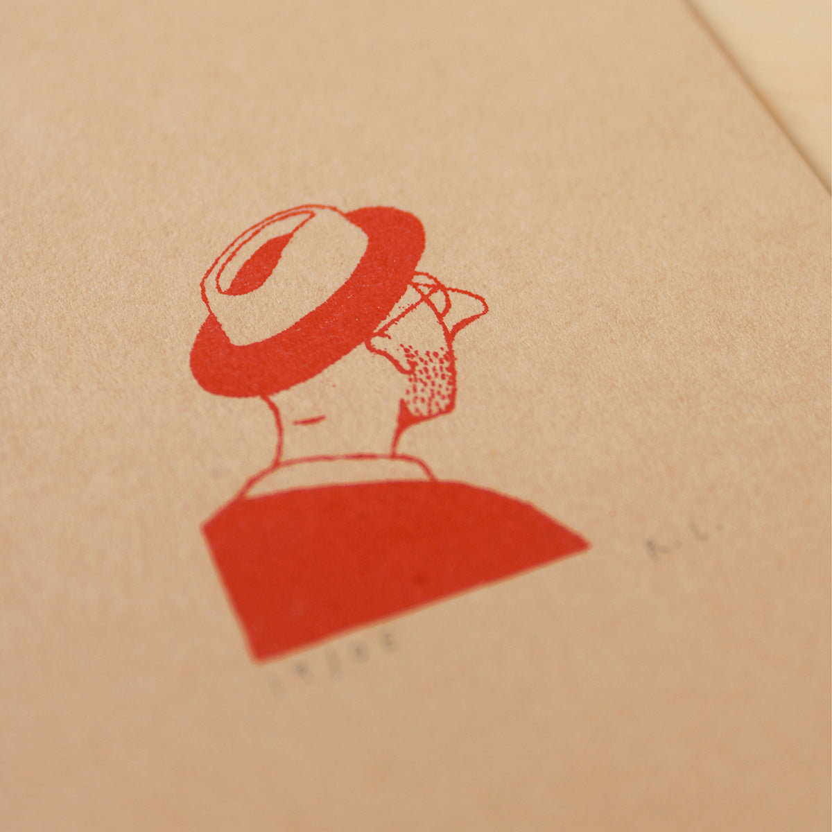 A close-up of a kraft paper surface with a red printed illustration of a person in profile wearing a trilby hat, with small faint text below.