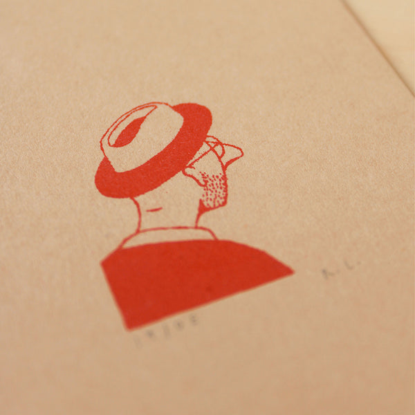 A close-up of a kraft paper surface with a red printed illustration of a person in profile wearing a trilby hat, with small faint text below.