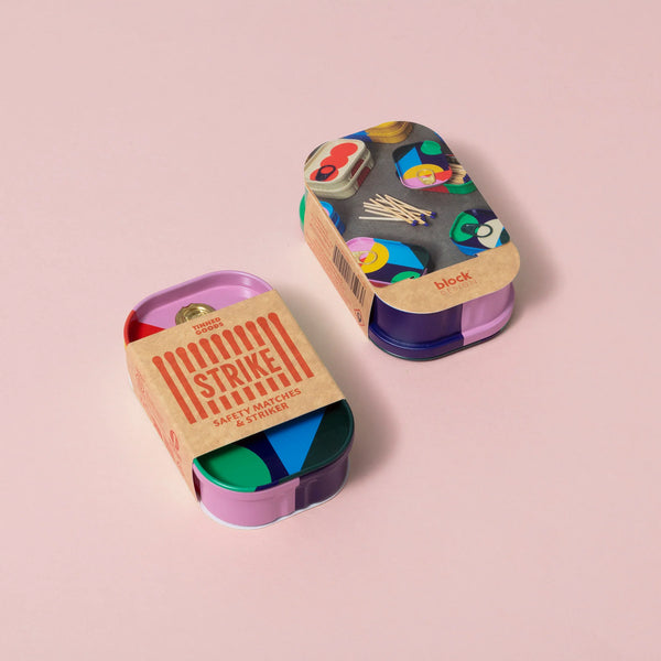 Coluorful matchbox tins with a cardboard label on a pink background