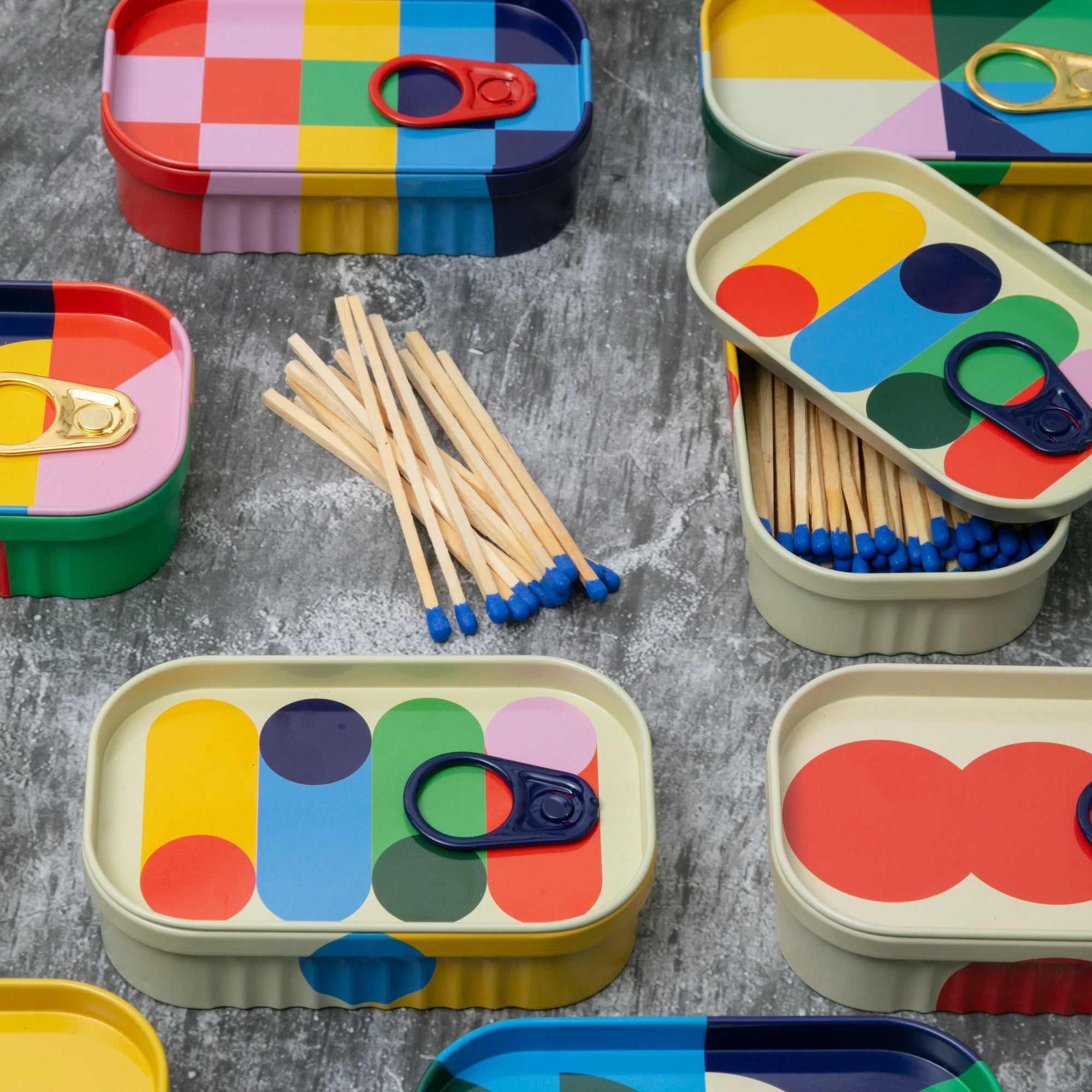Coluorful matchbox tins with matches on a grey surface